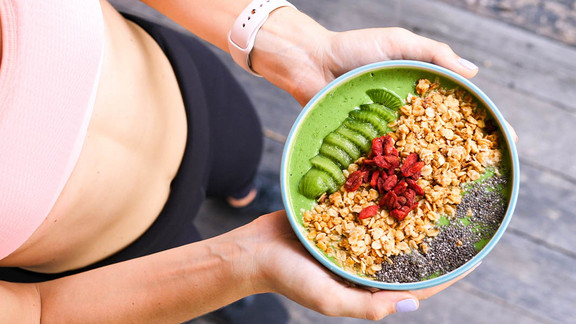 Eine Frau mit einer sportlichen Figur hält eine Bowl zum gesunden Abnehmen.